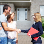 Happy couple shakes hands with a real estate agent in front of their newly purchased home