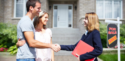 Happy couple shakes hands with a real estate agent in front of their newly purchased home