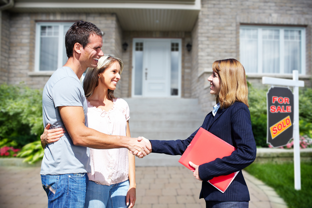 Happy couple shakes hands with a real estate agent in front of their newly purchased home