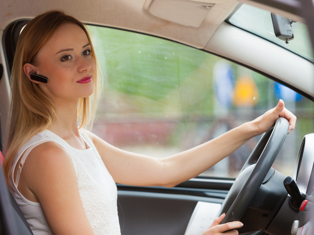 Young woman drives car safely using bluetooth ear piece for hands-free phone calls