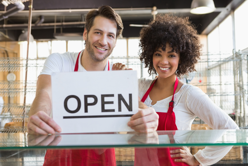 Smiling team posing behind the counter with open sign at the bakery