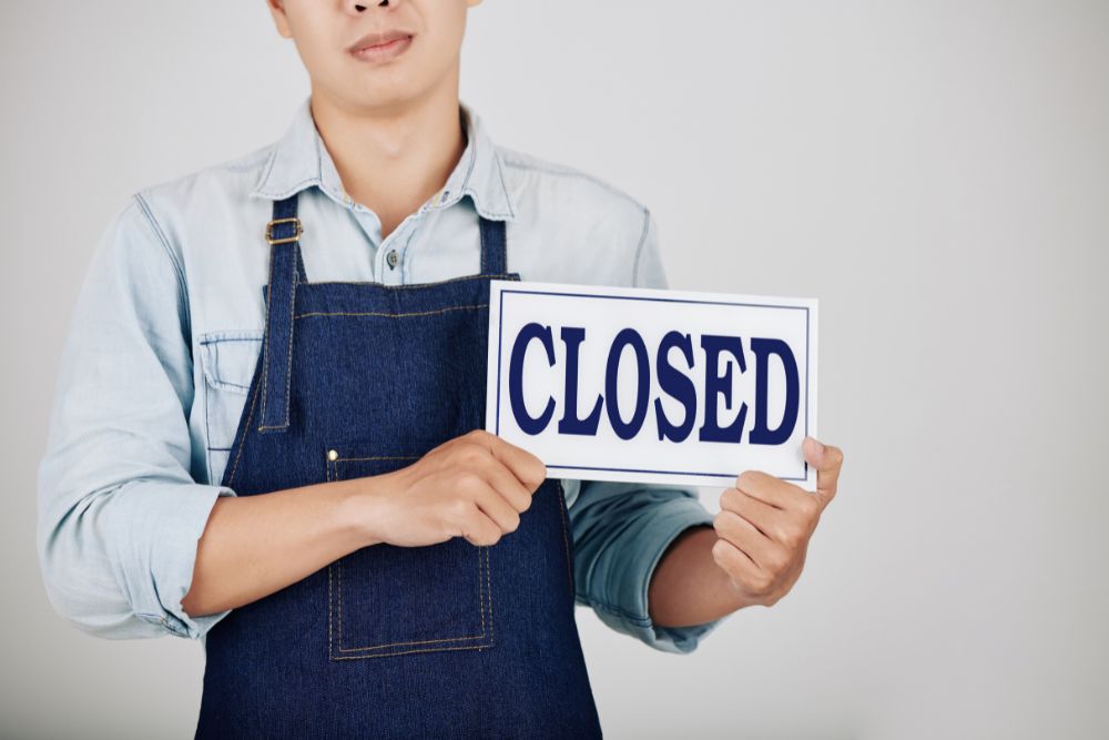 business owner holds closed sign