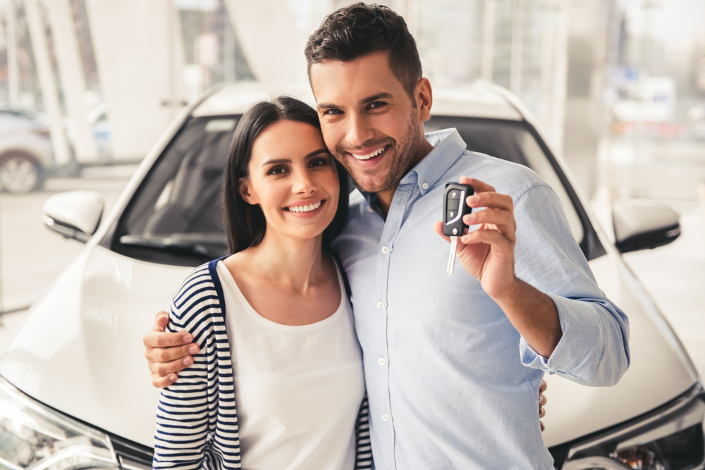 Beautiful couple is holding a key of their new car, looking at camera and smiling