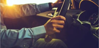 Driver holding steering wheel with sunlight streaming through windshield