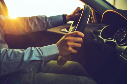 Driver holding steering wheel with sunlight streaming through windshield