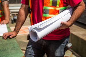 Construction worker in neon vest holding blue prints