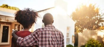 Couple with arms around each other looking at a house in the sunlight