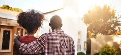 Couple with arms around each other looking at a house in the sunlight