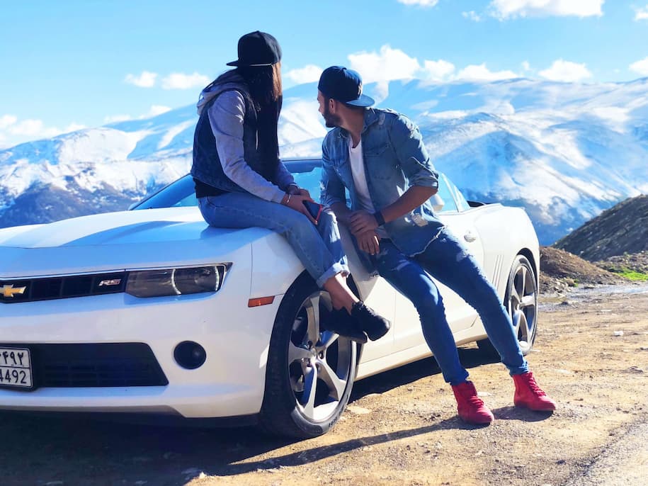 couples on white sports car by a snow covered mountainside