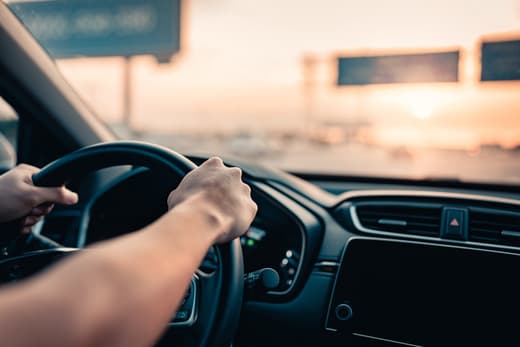 Driver holding steering wheel while driving at sunset on a highway