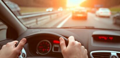 ands on steering wheel while driving in traffic at sunset