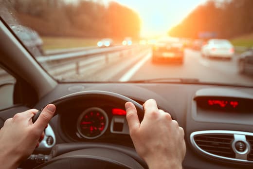 ands on steering wheel while driving in traffic at sunset