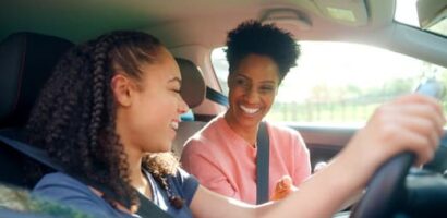 Adult teaching a teen how to drive inside a car