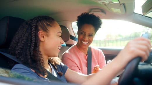 Adult teaching a teen how to drive inside a car