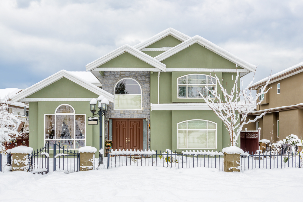 Green home with wrought iron fence covered in snow for the winter