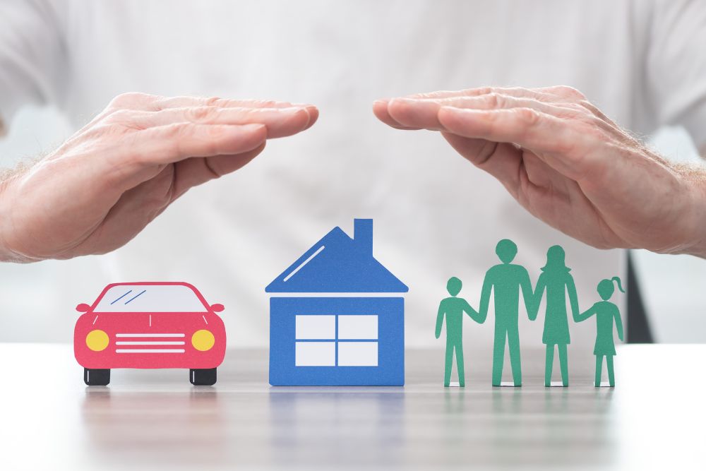 insurance broker's hands protect cut outs of car, home, and family