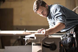 Man wearing denim shirt and black leather tool belt sands down a 2x4