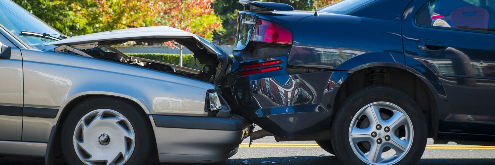 Older grey car rear ending a newer black car, causing damage to both vehicles.