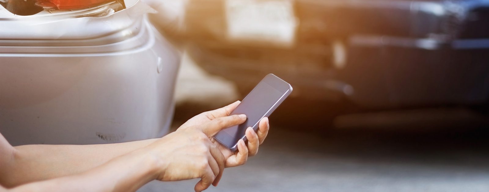 Person using smart phone standing behind the broken bumper of a grey vehicle