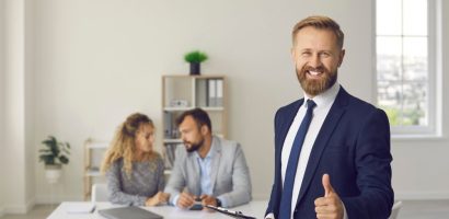 smiling insurance broker gives a thumbs up to the camera with clients in background