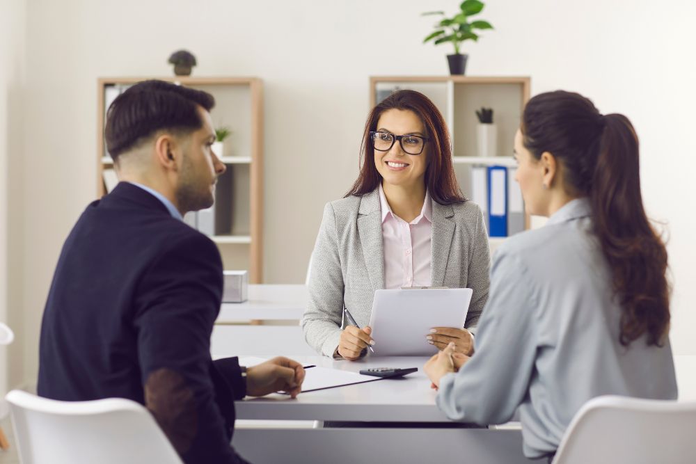 couple meets with female insurance broker, sitting at desk