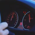 Driver’s hand on steering wheel with car speedometer showing mileage