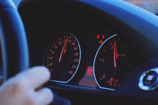 Driver’s hand on steering wheel with car speedometer showing mileage