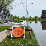 Orange sidewalk closed sign in front of flooded street