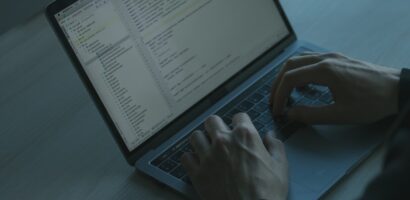 Person sitting in a dark room looks at website code on a laptop computer.