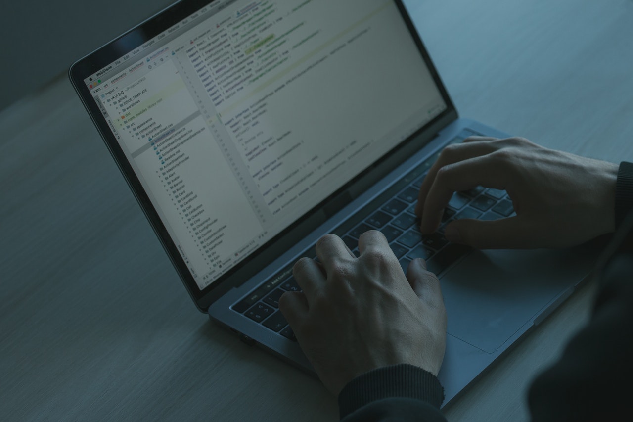 Person sitting in a dark room looks at website code on a laptop computer.