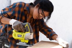 female contractor in blue and orange plaid shirt cutting plywood with a power saw