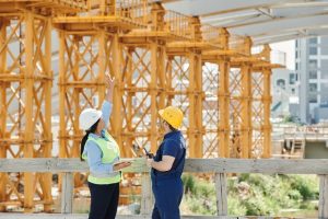 Man and woman in hardhats stand in front of yellow scaffolding 