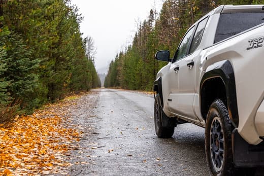Pickup truck parked on a quiet forest road with fallen autumn leaves