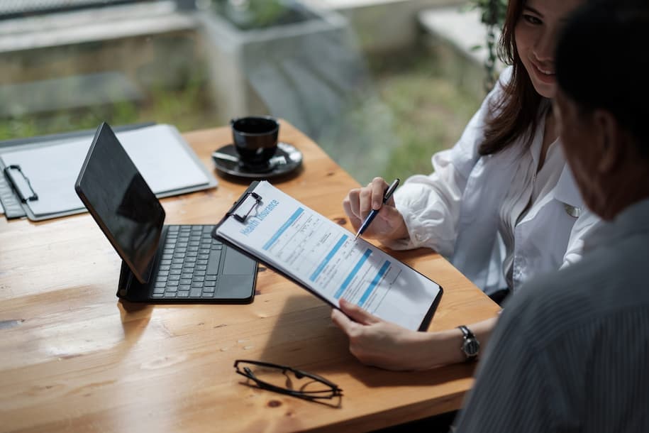 professional woman pointing her pen to health insurance form and showing it to another person