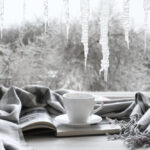 White mug on top of book wrapped in a grey blanket, with a wintery window scene in the background