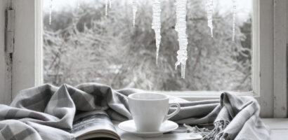 White mug on top of book wrapped in a grey blanket, with a wintery window scene in the background