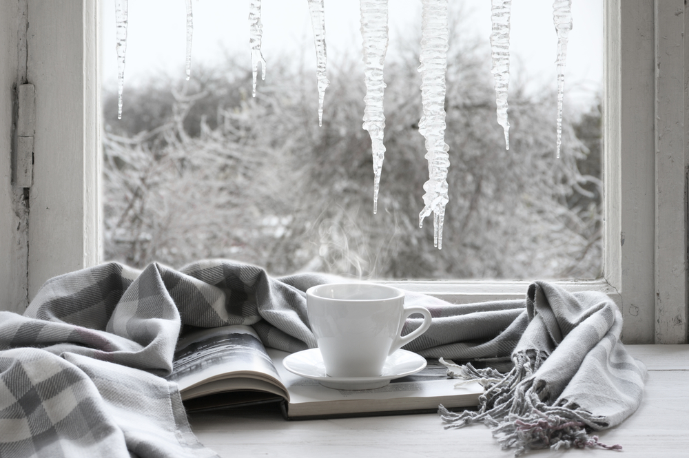 White mug on top of book wrapped in a grey blanket, with a wintery window scene in the background