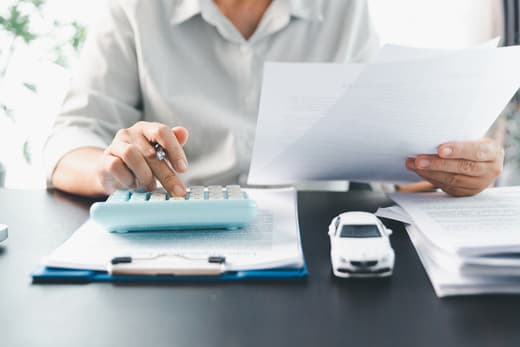 Person reviewing insurance documents and calculating costs at a desk with a model car