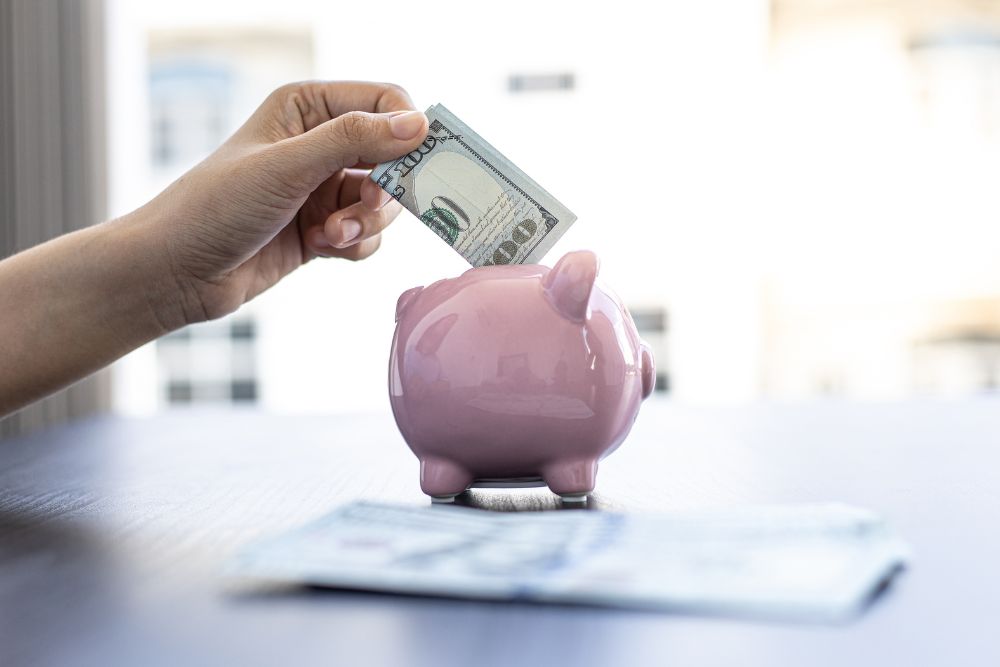 hand place 100 dollar bill into small piggy bank