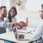 Three people sitting at a table shaking hands