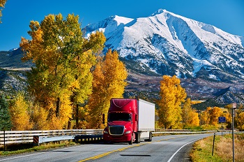 Red semi truck with white trailer driving through a scenic mountain range