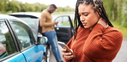 Woman checking her phone beside a stopped car after a roadside incident