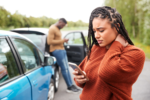 Woman checking her phone beside a stopped car after a roadside incident